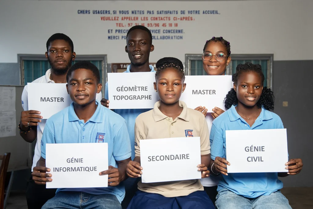 Groupe d’étudiants de l’ESGC-VAK tenant des pancartes : Master, Géomètre Topographe, Génie Informatique, Secondaire, Génie Civil