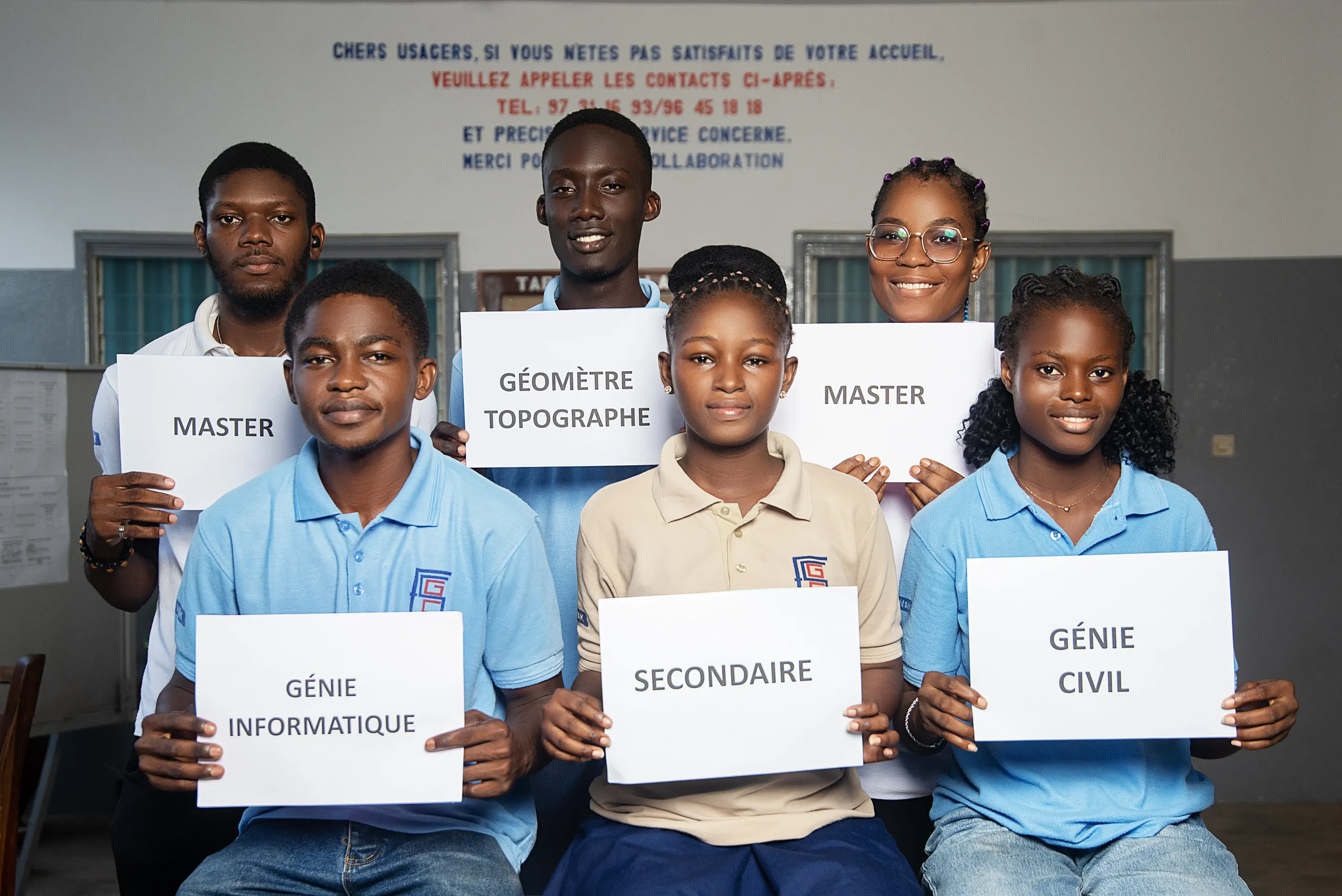 Groupe d’étudiants de l’ESGC-VAK tenant des pancartes : Master, Géomètre Topographe, Génie Informatique, Secondaire, Génie Civil