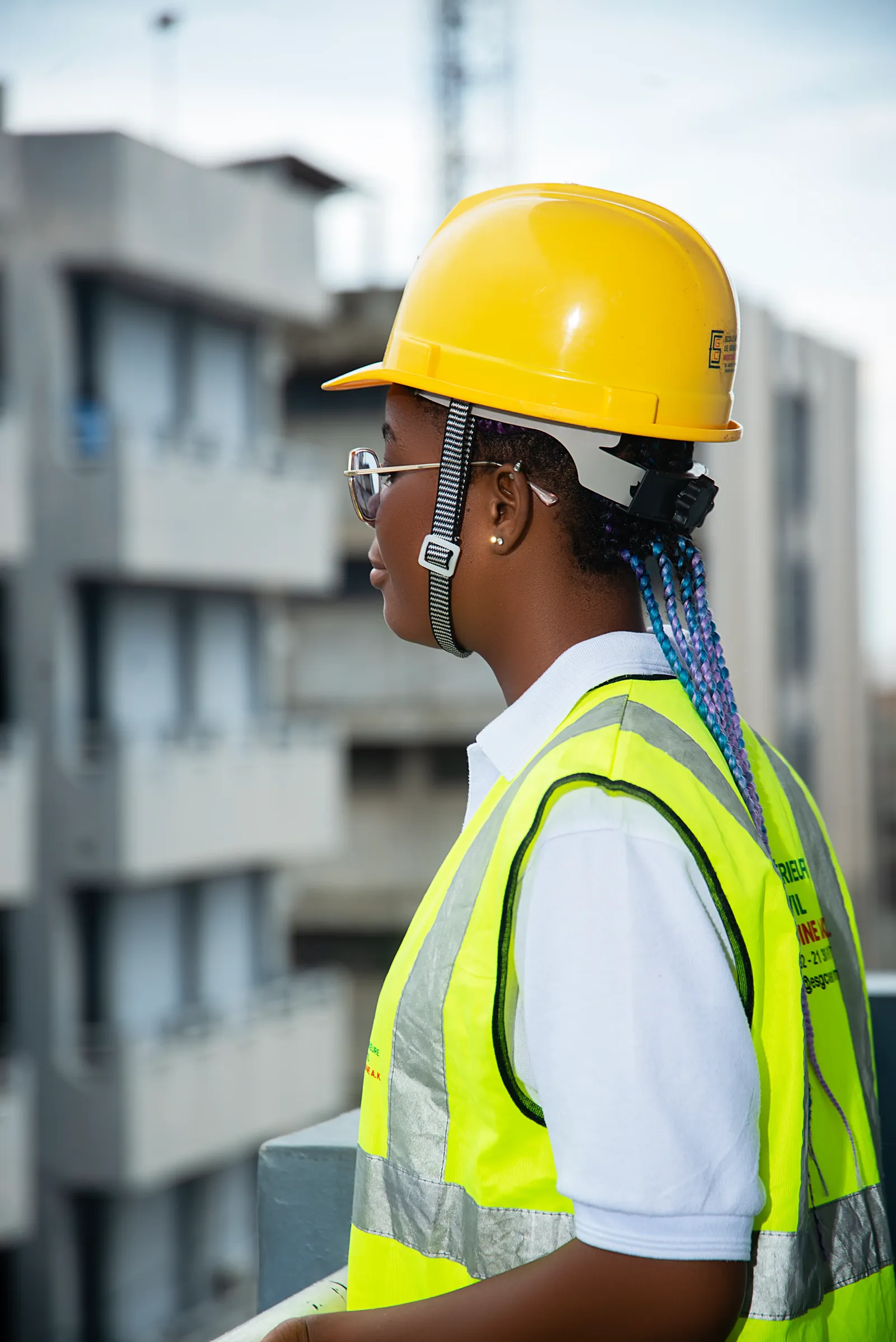 Étudiante en casque jaune et gilet de sécurité, de profil, sur un chantier