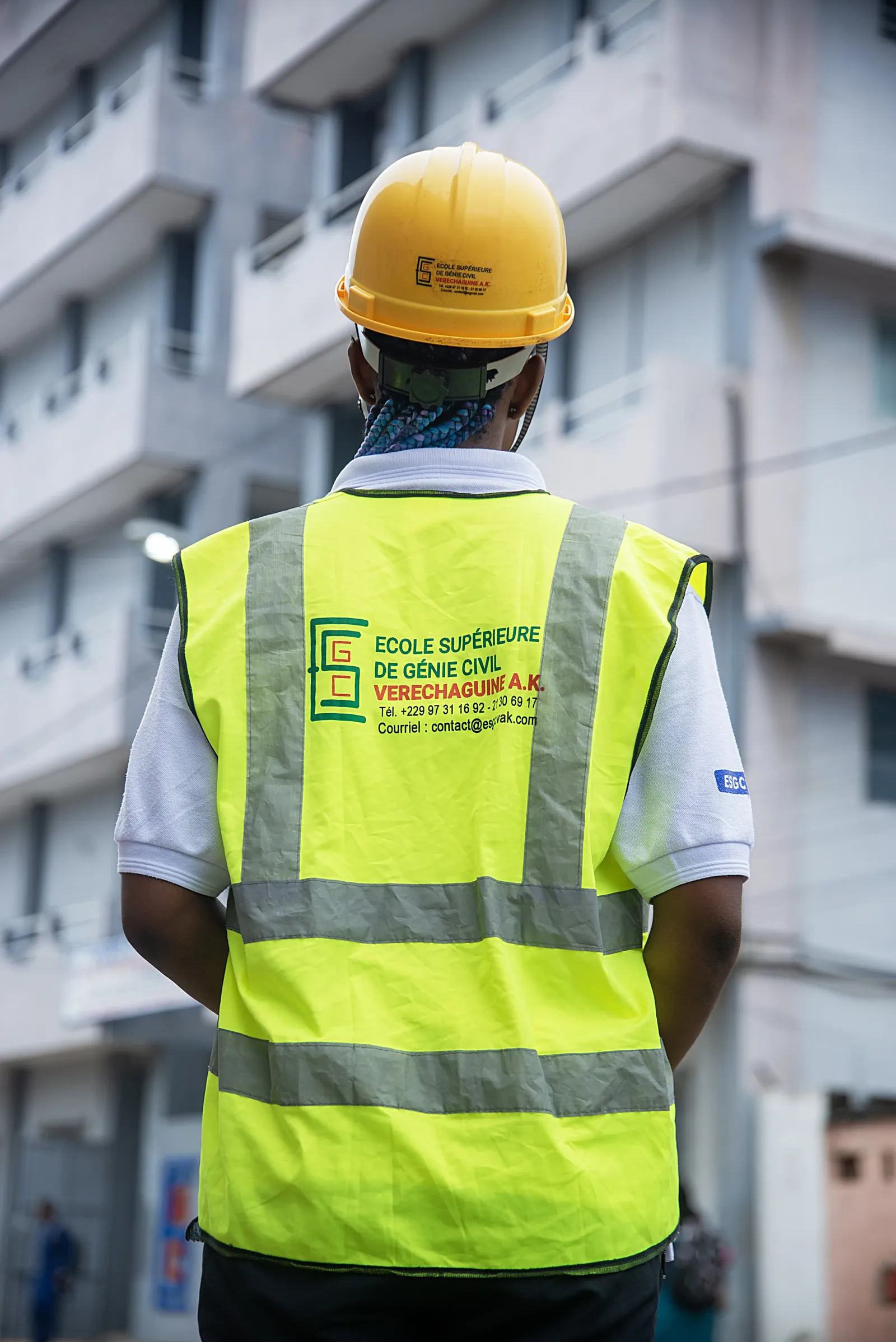Étudiante en casque jaune, de dos, portant un gilet de sécurité aux couleurs de l’ESGC-VAK