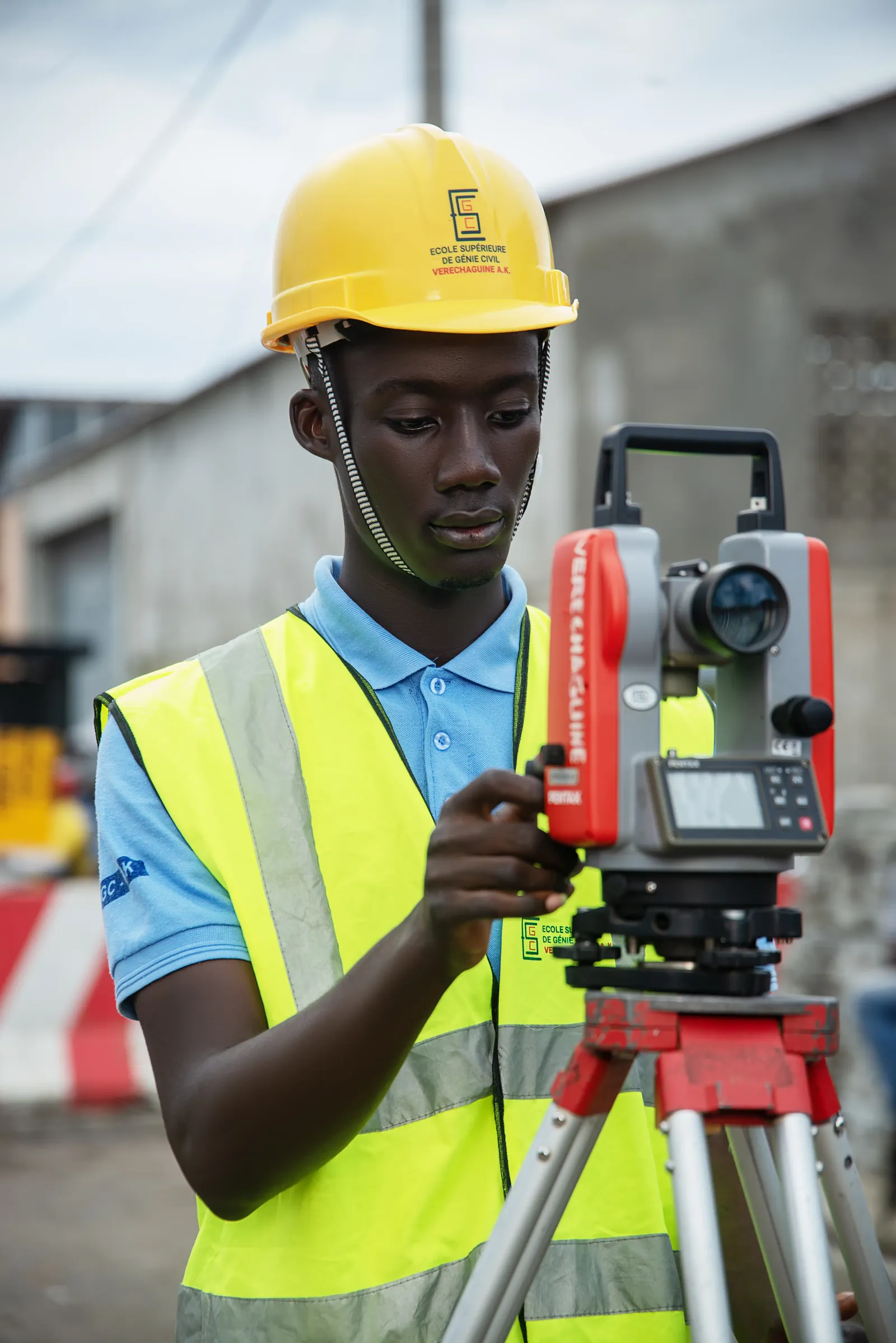 Étudiant en casque jaune réglant un théodolite sur un chantier